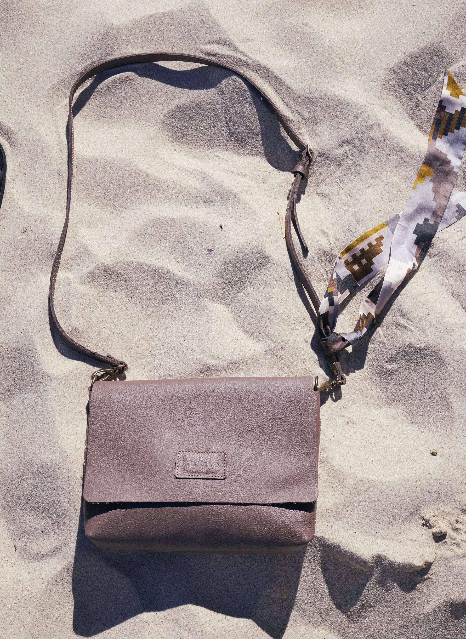 Taupe handbag on sand with a patterned twilly
